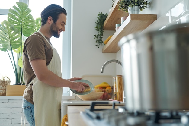 Foto een knappe jonge man die afwas doet in de keuken.