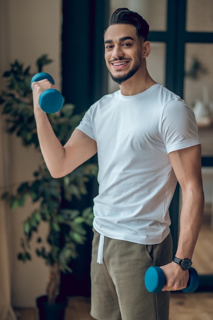 Een knappe jonge man die oefent met dumbbells.