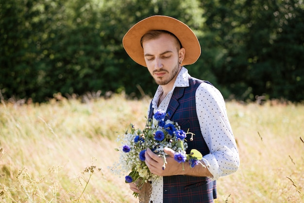 Een knappe jonge man met een baard en een hoed in het veld met een boeket bloemen