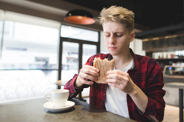 Een knappe jonge man met een eetlust te kijken naar een broodje in zijn handen