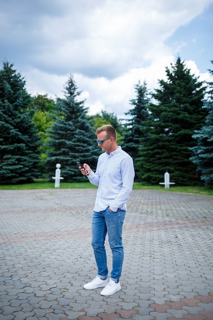 Een knappe jonge man van Europees uiterlijk die een zonnebril draagt, is gekleed in een shirt en spijkerbroek. De man loopt over straat, hij is stijlvol gekleed