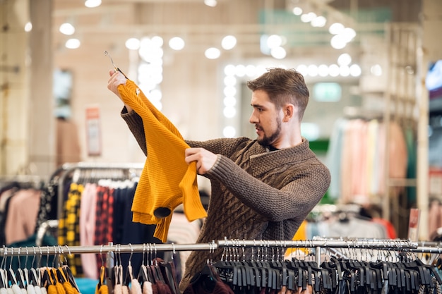 Een knappe jonge mens die kleding in een detailhandel kiest