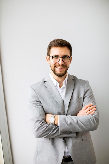Een knappe jonge moderne zakenman die bij de muur in het kantoor staat.