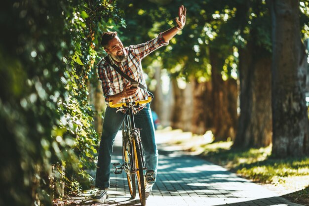 Een knappe jongeman gaat met zijn fiets naar de stad, zit erop en zwaait naar iemand.