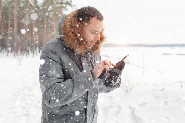 Een knappe jongeman gebruikt een mobiele telefoon in een besneeuwd bos.