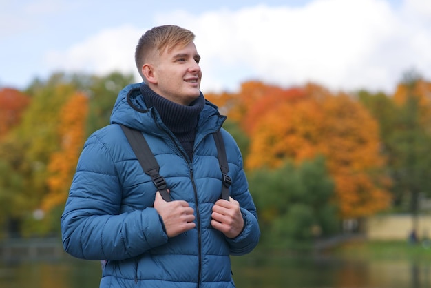 Een knappe jongeman wandelt in het gouden herfstpark op een prachtige meerachtergrond met