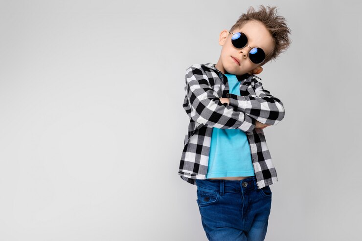 Een knappe jongen in een geruit hemd, blauw shirt en spijkerbroek staat. De jongen draagt een ronde bril. Roodharige jongen sloeg zijn armen over zijn borst