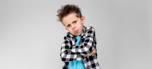 Een knappe jongen in een geruit hemd, blauw shirt en spijkerbroek staat. De jongen sloeg zijn armen over zijn borst. De jongen toont de taal