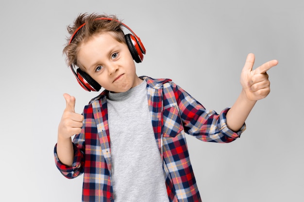 Een knappe jongen in een geruit hemd, grijs shirt en spijkerbroek staat. Een jongen in een rode koptelefoon. De jongen wijst met zijn vingers naar de zijkant.