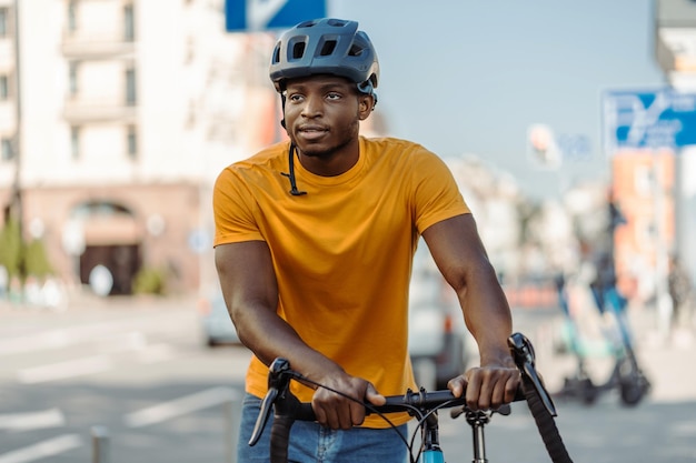 Een knappe lachende Afro-Amerikaanse man met een helm die op een fiets rijdt en wegkijkt.