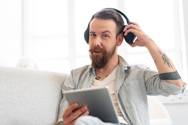 Een knappe man met een baard die een digitale tablet gebruikt terwijl hij thuis op de bank rust.