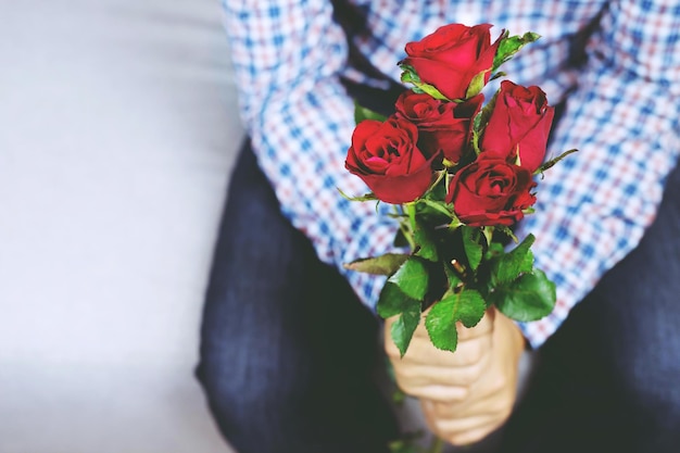 Een knappe man met een geruit overhemd, zittend op de bank, houdt Boeket van mooi met rode roze bloem vast