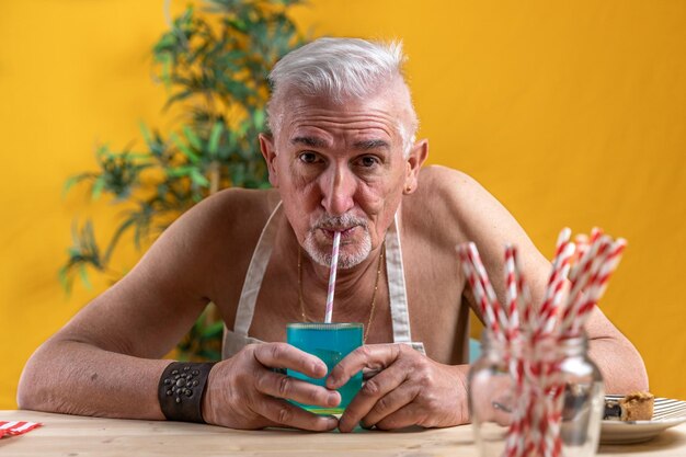 Foto een knappe man van middelbare leeftijd die aan tafel zit en een blauwe frisdrank door een rietje drinkt.