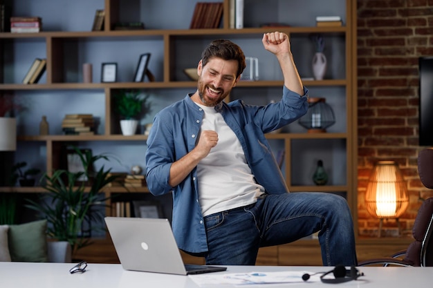 Een knappe mannelijke zakenman voltooide zijn baan met succes en begon met plezier te dansen in zijn thuiskantoor Dansende manager freelancer aan het einde van de werkdag na een succesvol project