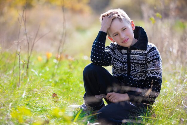 Een knappe rustige jongen in een gebreide trui zit op het gras op het veld