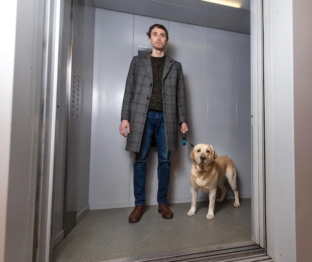 Een knappe stijlvolle man die met een labrador in de lift staat.