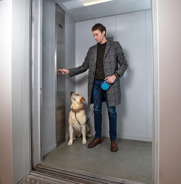 Een knappe stijlvolle man die met een labrador in de lift staat.