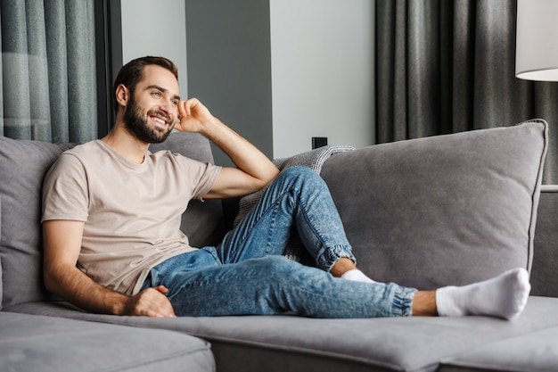 een knappe vrolijke jonge positieve man binnenshuis zit op de bank.