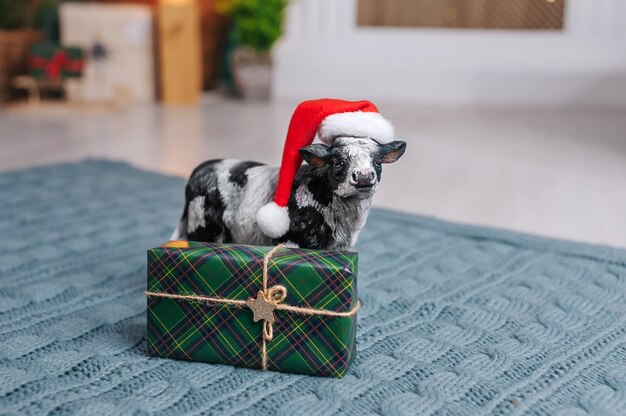 Een koe met een oudejaarsmuts draagt een slee met cadeautjes tegen de achtergrond van het interieur