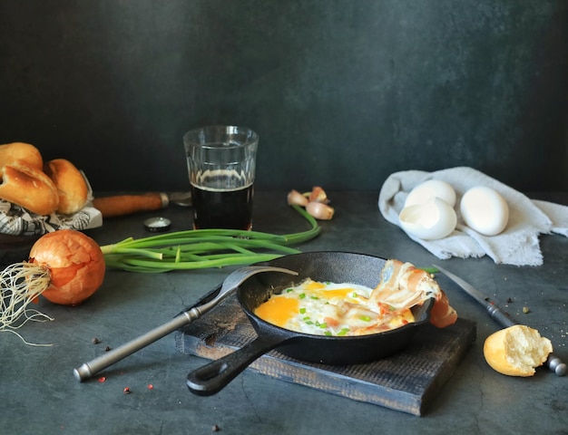 Een koekenpan met roerei en spek en bier op de keukentafel thuis Eten en drinken