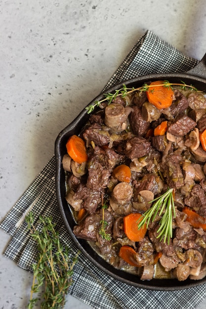 Een koekepan met rundvlees bourguignon met worstjes, wortelen, knoflook, ui, rode wijn, kruiden en specerijen.