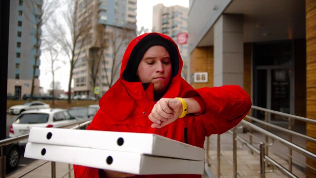 Een koerier die pizza bezorgt die op straat loopt en naar het horloge kijkt