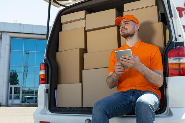 Een koerier met een tablet in zijn handen bij een auto met dozen