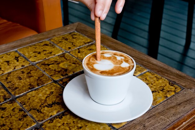 Een koffiekop Latte die door pijpjes kaneel wordt geroerd.