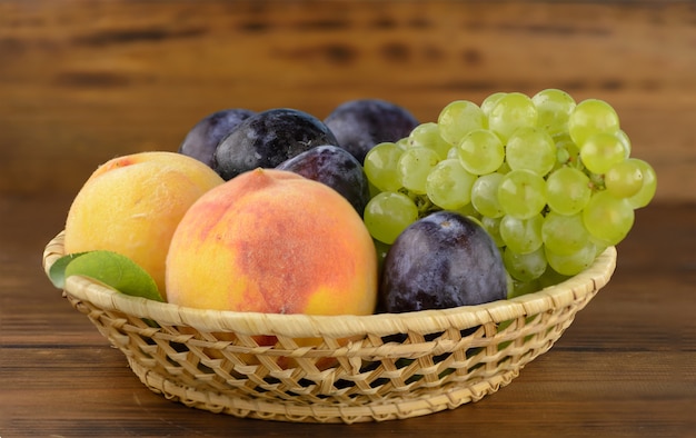 Een kom met smakelijke, rijpe zomer fruit op de bruine houten tafel.