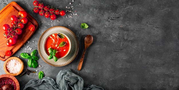een kom traditionele Spaanse tomatensoep met room en basilicum op de grijze tomaat als achtergrond en