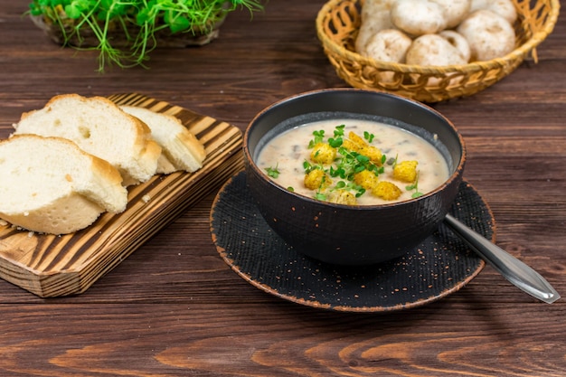 Een kom zelfgemaakte champignonpureesoep met kruiden en brood op een houten tafel Zelfgemaakte vegetarische champignonsoep met groenten en brood