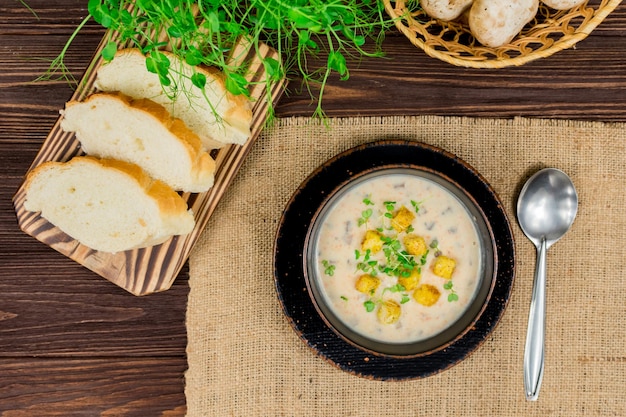 Een kom zelfgemaakte champignonpureesoep met kruiden en brood op een houten tafel Zelfgemaakte vegetarische champignonsoep met groenten en brood