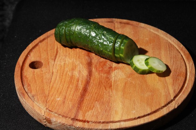 Foto een komkommer op een houten snijplank waar een plakje uit is gesneden.