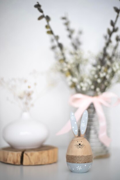 Een konijnenbeeldje zit voor een vaas met bloemen op de achtergrond.