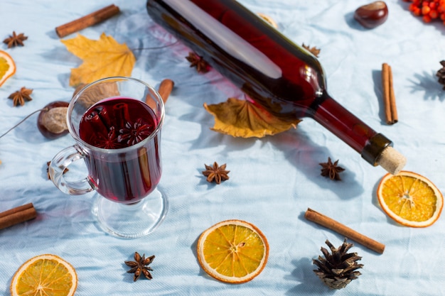 Een kop glühwein met kruiden, fles, droge bladeren en sinaasappelen op tafel. Herfststemming, methode om warm te blijven in de kou, copyspace, ochtendlicht.