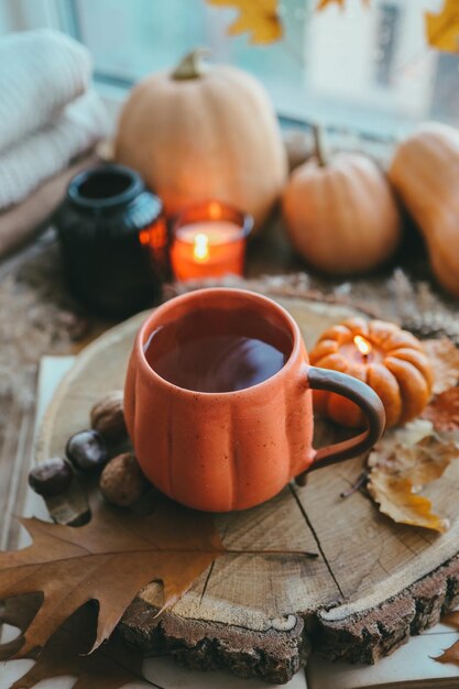 Een kop hete dampende thee en een pompoenvormige kaars op de vensterbank herfststemming