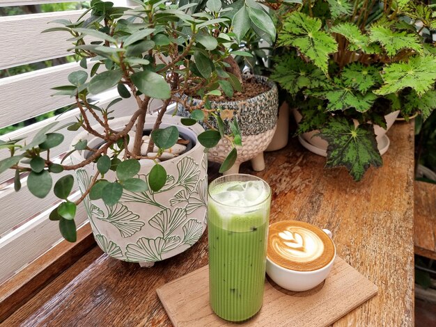 Een kop hete latte art koffie en iced green tea latte op een houten bord