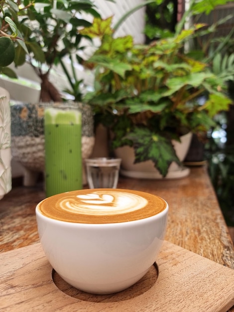 Een kop hete latte art koffie op een houten bord en een ijsthee groene thee latte en drinkwater