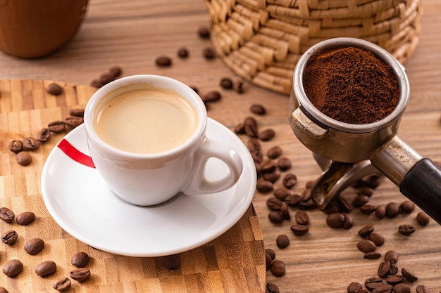 Een kop koffie met een rood handvat staat op een tafel naast een stapel koffiebonen.