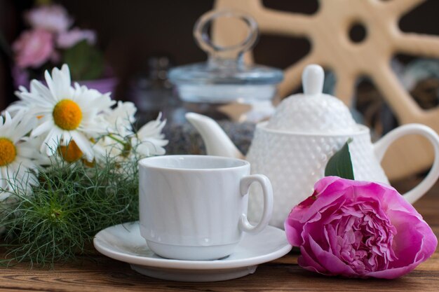 Een kop thee en een theepot met een roos op een houten achtergrond met een houten wiel Het concept van ontbijt in het dorp