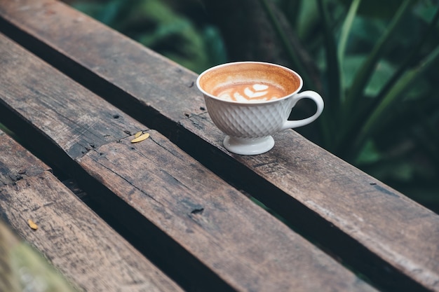 Een kop van hete lattekoffie met hart latte kunst op houten bank op groene aardachtergrond