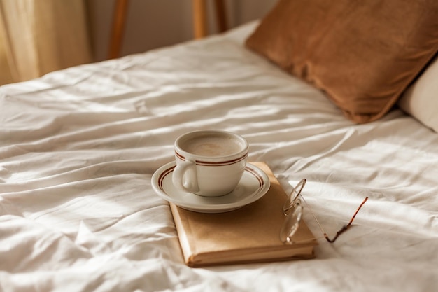 Een kop warme cappuccino een boek een bril op bed Ontbijt Gezellig huis Decordetails