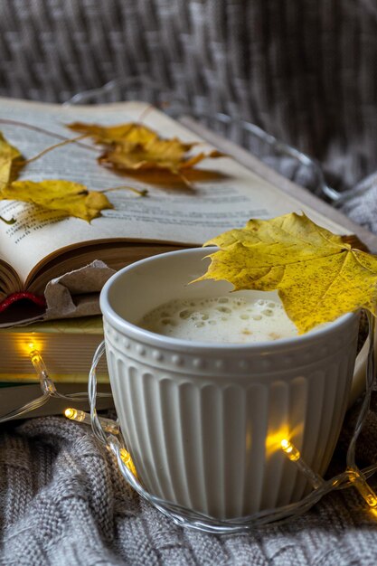 Een kop warme koffie, een stapel boeken en gele esdoornbladeren op een gebreide plaid