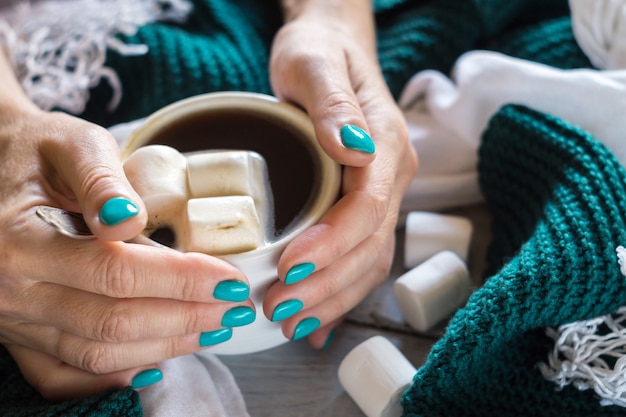 Een kopje cacao met marshmallow in vrouwelijke handen met een blauwe manicure