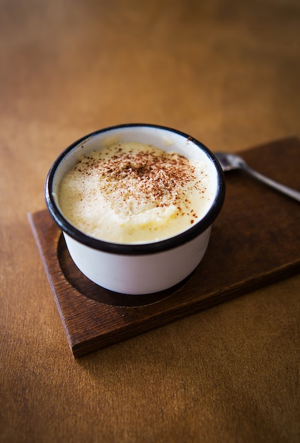 Een kopje cappuccino staat op een houten tafel en staat voor een lepel