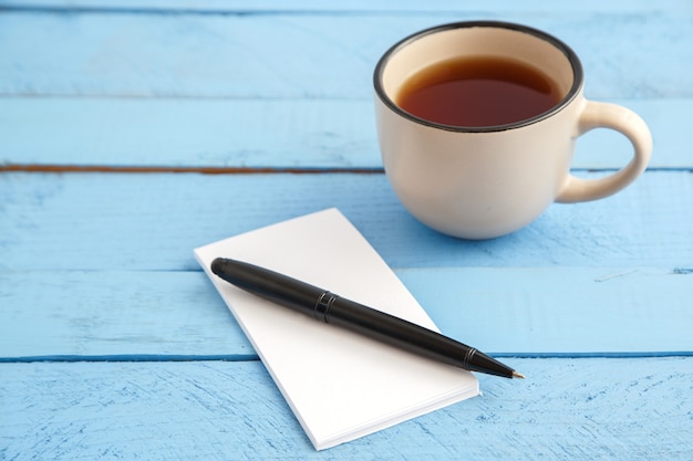 Een kopje drank en een papieren notitieblok met een zwarte pen op een blauw hout