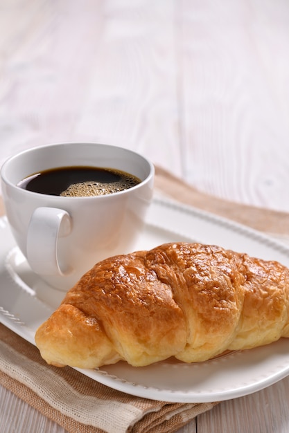 Een kopje koffie en een croissant op houten tafel