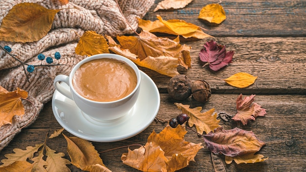 Een kopje koffie en herfstgebladerte op een bruine houten ondergrond