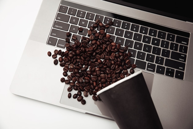 Een kopje koffie en koffiebonen op toetsenbord aan het witte bureau.