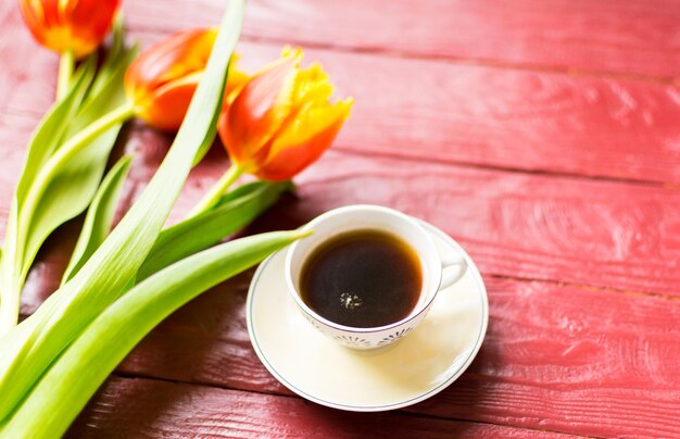 Een kopje koffie en tulpen op een bordeauxrode houten achtergrond